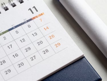 Overhead flat-lay of a table calendar with a metallic foil accent, next to a rolled banner, sharp studio lighting.