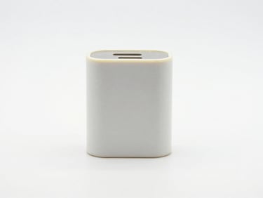 Centered, straight-on studio shot of a cheap plastic wall charger on a clean white background, showing slight yellowing and misaligned seams, bright even lighting.