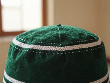 Close-up macro shot of reinforced stitching on a premium prayer cap, warm diffused mosque light