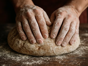 Tactile macro shot of a baker's hands covered in white flour, kneading rustic sourdough on a dark wooden table, soft side daylight, shallow depth of field.