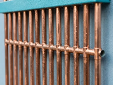 Modern copper plumbing pipes arranged neatly against a wall, bright daylight, sharp focus on clean solder joints