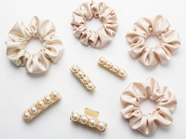 Clean flat lay of assorted pearl hair clips and satin scrunchies on a pristine white background, bright studio lighting, sharp focus.