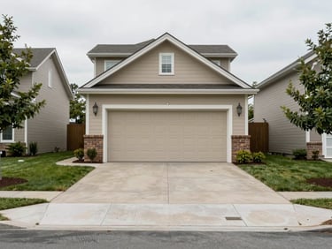 Wide shot of a cleared residential driveway and closed garage door from street level, clean suburban yard, overcast diffused light, no vehicles or people