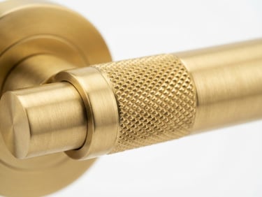 Macro studio shot of solid brass door hardware with a brushed gold finish, sharp focus on machined knurling, crisp white background, high-key lighting.