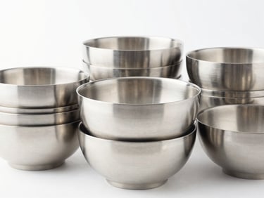 A stack of minimalist polished stainless steel bowls and cookware, high-key studio lighting, crisp reflections, clean background