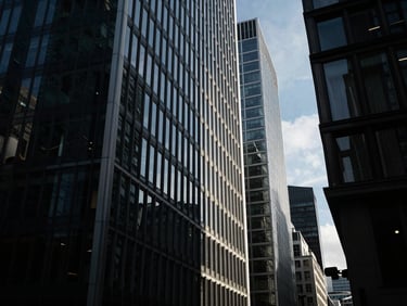 Extreme wide-angle environmental shot of modern London steel-and-glass skyscraper sliced by sharp morning sunlight and deep obsidian shadows.