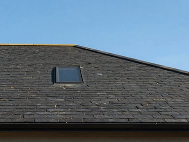 Straight-on architectural elevation of a modern dark slate roof against a bright blue sky, sharp shadows