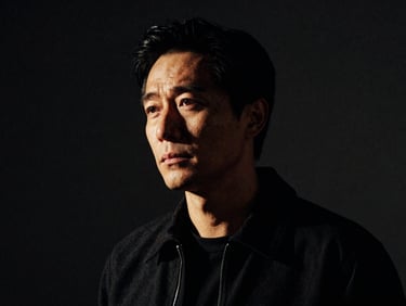 High-contrast character portrait of a male director in a dark studio, dramatic side-lighting, deep shadows, gritty 35mm grain.