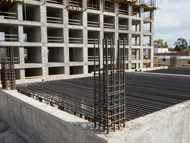 Wide shot of concrete formwork being assembled on a multi-storey residential building site, rebar lattice visible inside the pour zone, daylight, active construction phase, no finished surfaces