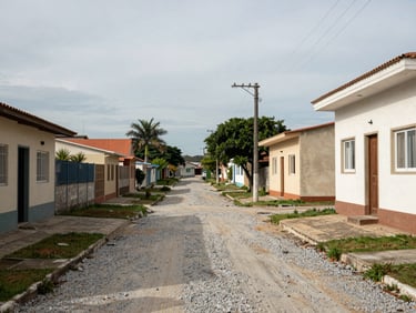 Street approach to a residential lot in Navegantes, gravel path, neighboring low-rise buildings visible, overcast morning light, no vehicles blocking view