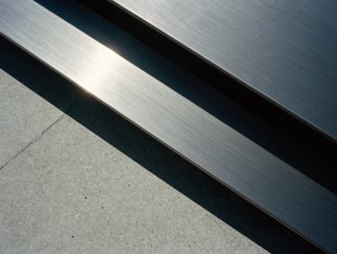 High-contrast editorial close-up of premium textured concrete and brushed steel, stark diagonal shadows, cool overcast daylight, medium format film.