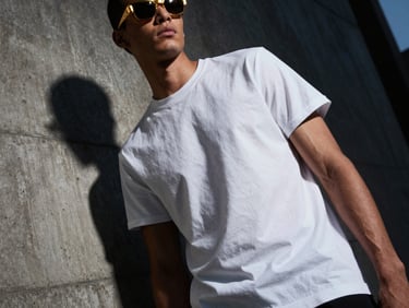 Low-angle dynamic shot of a model in a boxy white t-shirt, concrete background, harsh side shadows.