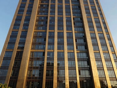 Wide-angle view of a modern Gurugram high-rise facade, golden hour sunlight reflecting off glass, deep navy and gold tones, symmetrical composition.
