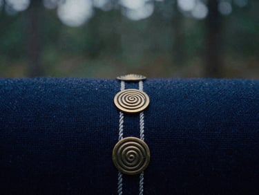 Close-up of hand-woven dark indigo wool fabric with bronze spiral ornaments, moody natural overcast light, 35mm film grain
