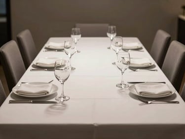 Wide-angle view of a polished corporate dinner table set for twelve, crystal glassware and white linen, soft directional light from above, no people present