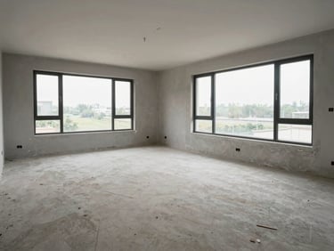 Wide shot of an empty newly completed residential unit — bare concrete floors, unpainted walls, large window framing site context outside, north-facing natural light, no furniture or people — the spatial intention readable without any staging