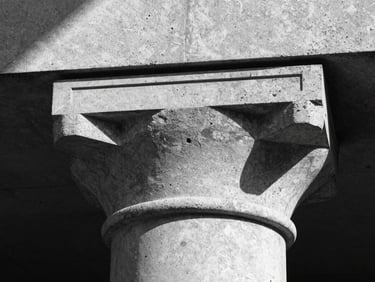 Sharp architectural detail of a brutalist column capital in polished concrete, directional key light casting a single hard shadow across the surface, monochromatic study, no figures