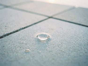 Macro photograph of clean water reflecting soft morning light on a light gray stone tile, shallow depth of field, 35mm