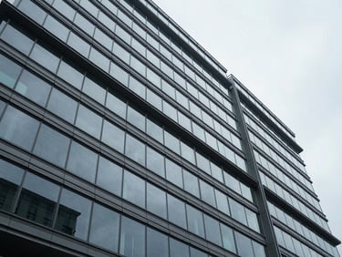 Wide architectural perspective of a modern glass and steel corporate facade, sharp geometric angles, cool overcast daylight, minimal composition.