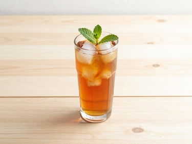 A tall glass of iced amber tea with a sprig of mint on a sunlit birch wood table, soft shadows