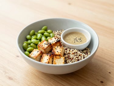 A vibrant grain bowl with roasted tofu, green edamame, quinoa, and a light sesame dressing under soft daylight