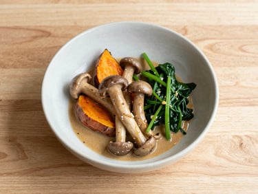 A clean ceramic bowl of wild mushrooms, roasted sweet potato, spinach, and savory miso sauce, top-down view