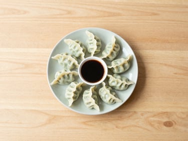 A small ceramic plate of steamed vegetable dumplings with dipping sauce, top-down minimalist composition