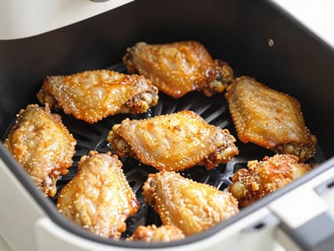 Close-up of golden crispy chicken wings in an air fryer basket, bright kitchen light, glistening texture