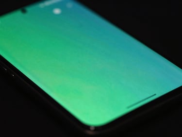 Macro close-up of a physical Android screen displaying fluid UI transitions, dark studio background, vibrant green and teal neon reflections, 35mm
