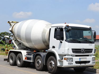 Low-angle heroic shot of a concrete mixer truck discharging ready-mix concrete on a bright Alagoas construction site, high contrast, gritty texture, 35mm lens