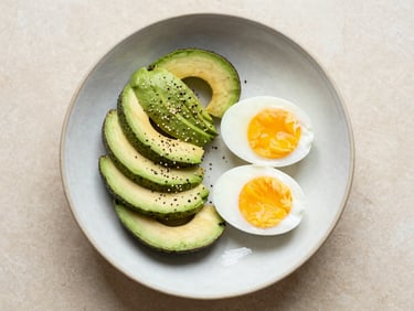 Overhead flat lay of a simple healthy bowl with fresh avocado, eggs, and seeds on a rustic ceramic plate, soft morning daylight