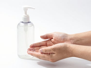 Front-facing studio shot of a handwash bottle next to clean hands, bright clinical lighting