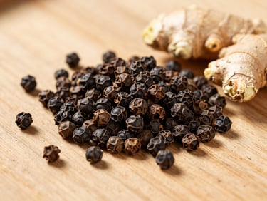 Close-up of premium black peppercorns and dried ginger roots on a rustic wooden surface, warm natural light, warm editorial photography, bright natural daylight, rich organic earth tones, clean composition, shallow depth of field, 35mm