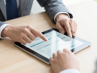Close-up of a professional consultation, hands pointing at a tablet showing insurance documents on a wooden desk, bright natural daylight, shallow depth of field