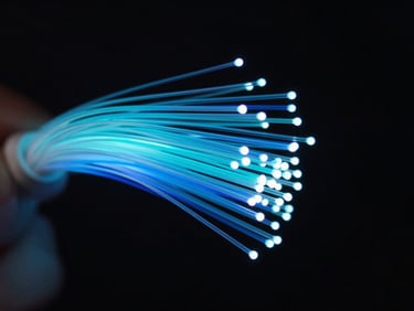 Wide macro shot of fiber optic strands fanning out in blue and cyan light against a black background, shallow depth of field, cold studio lighting