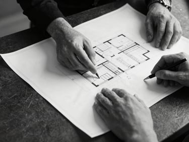 Monochrome close-up of executive hands reviewing physical architectural blueprints on a dark slate table, sharp side-lighting, high contrast