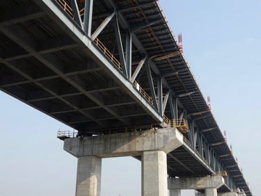 Low-angle view of a large bridge under construction, steel girders and concrete pillars, sharp daylight, wide-angle lens, high contrast