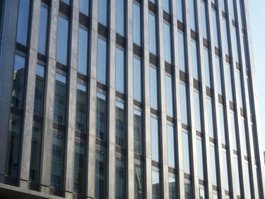 Wide environmental shot of a modern corporate office building facade with clean lines and reflective glass, bright natural daylight, 35mm lens