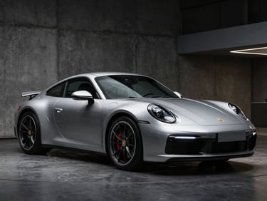 Sleek Porsche 911 Carrera in a dark modern concrete showroom, three-quarter angle, low-key lighting reflecting off metallic silver paint, 50mm lens