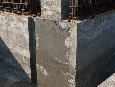 Close-up of a massive wet concrete pour on a heavy structural foundation, high-contrast morning light highlighting the texture of the concrete and steel rebars.