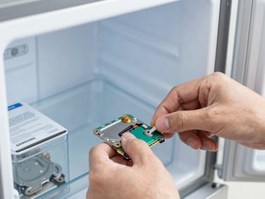 Macro shot of a technician's hands working on the internal components of a Samsung refrigerator, genuine spare part in original packaging visible, sharp focus.