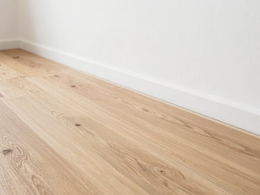 Close-up of newly installed wide oak floorboards meeting a minimalist white wall, bright natural daylight, clean lines, 35mm lens