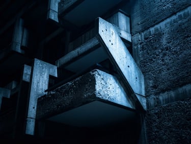 Wide, low-key, high-contrast shot of brutalist architectural concrete, stark geometric forms under harsh blue light, 35mm macro lens.