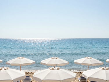 Wide environmental shot of Eforie beach with white umbrellas, calm turquoise sea, bright midday sun reflecting on water