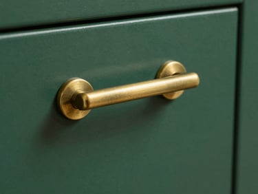 Close-up of a matte brass cabinet pull handle mounted on a deep-green lacquered cabinet door, studio even lighting, shallow depth of field showing metal texture and finish, no people, tight product framing