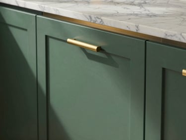Close-up detail shot of a premium modular kitchen island surface in situ — brushed gold cabinet pull hardware against a deep forest-green lacquered door panel, Calacatta marble countertop edge catching even north-facing natural light, a subtle solar-powered under-cabinet lighting strip glowing warm amber, no people, precise architectural product framing, landscape orientation