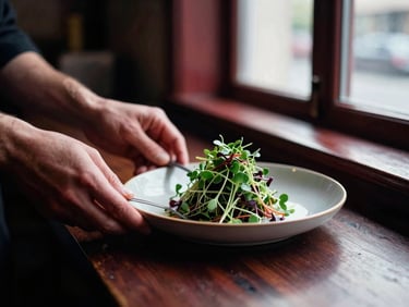 Hands plating a delicate microgreen salad in a moody Scandinavian-style restaurant kitchen, soft side window light, high-contrast shadows, rich crimson tones, 35mm film.