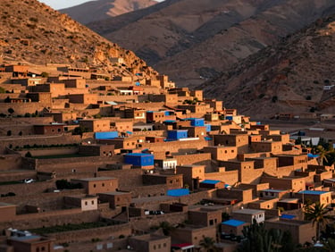 Terraced agricultural fields in a deep Moroccan mountain valley, ancient stone houses clustered on the hillside, warm morning window light, shallow depth of field