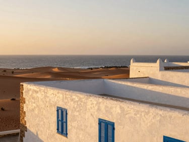 The whitewashed stone walls and blue shutters of Essaouira overlooking the Atlantic coast at sunset, golden-hour light