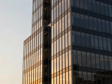 Modern corporate architecture facade in São Paulo, sharp glass angles reflecting warm golden hour sunset light, clean lines, professional 35mm editorial photography